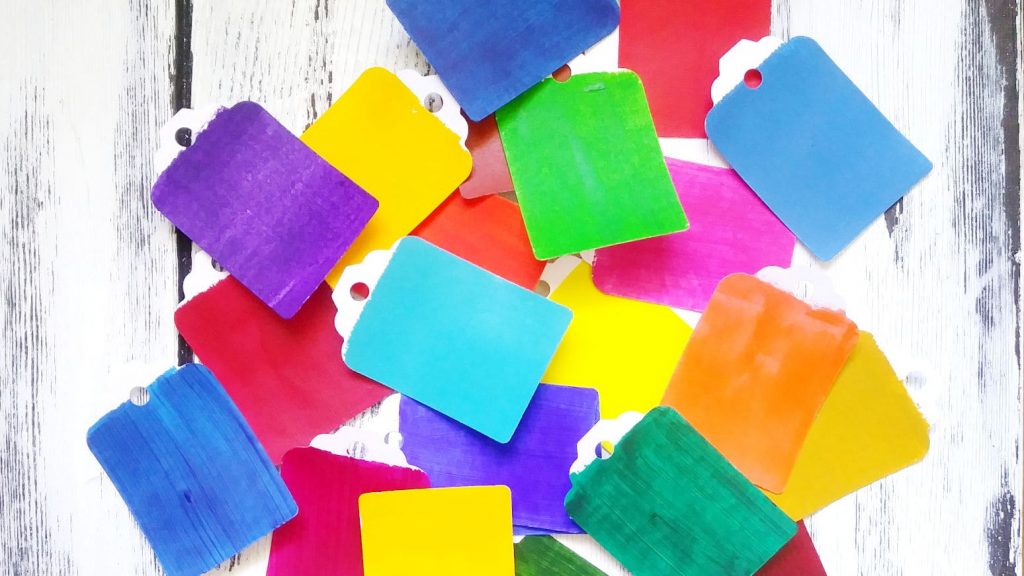 A pile of paint chips in every color of the rainbow against a whitewashed wooden background.
