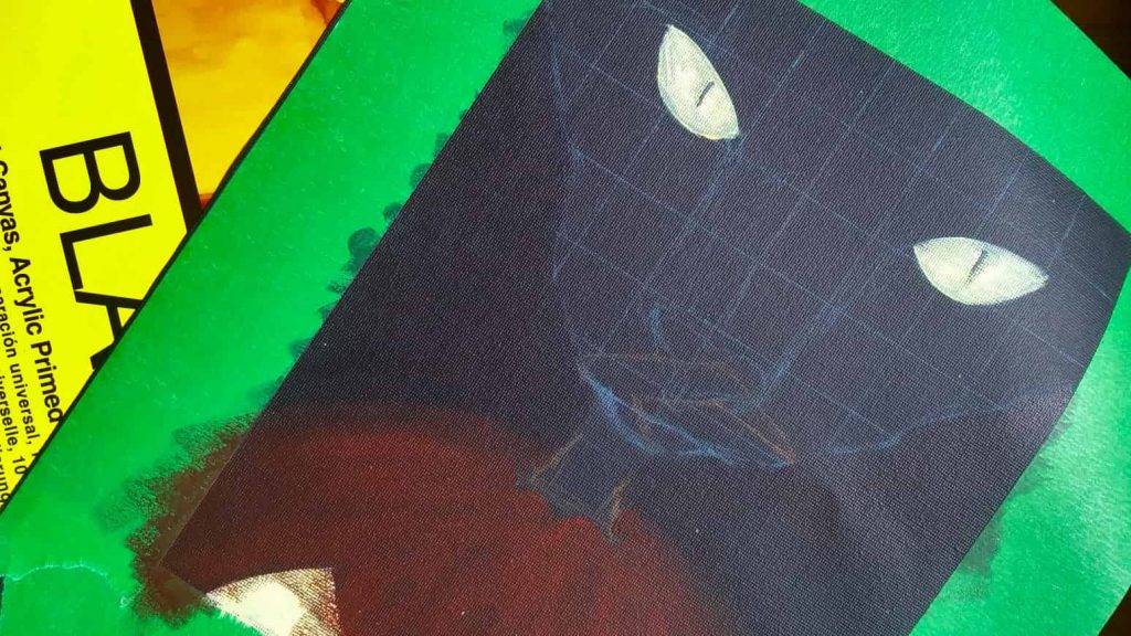 A painting in progress of a black cat and jack-o'-lantern on a black canvas. In the background is a Fredrix Black Canvas Pad.