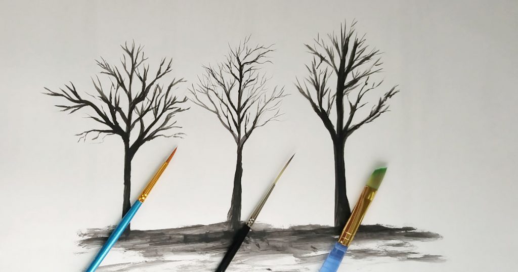 Three black trees with skinny limbs and the paintbrushes that were used to paint them.
