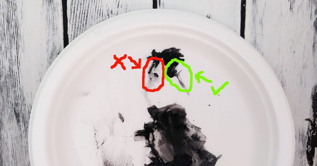 Black paint on a white palette that's been thinned with water to show how thin your paint should be when you want to paint thin sticks and twigs.