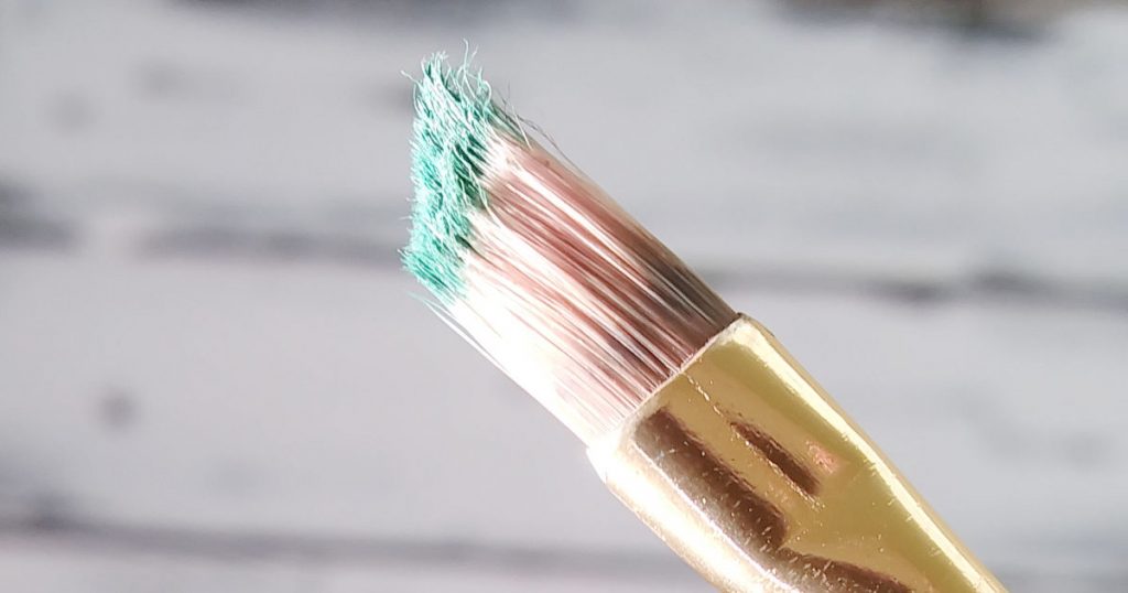 A very scruffy looking paint brush with a very small amount of green paint on the ends of the bristles to show how to prep your brush for the dry-brushing technique