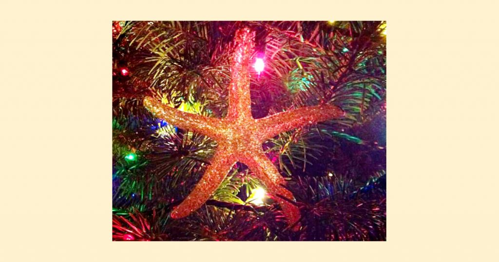 A close up of a sparkly gold starfish ornament hanging on a tree with multi-colored lights that show the type of glow you might want to add to make an easy Christmas tree painting a bit more interesting