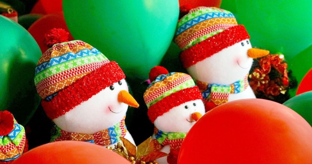 Three snowmen, wearing brightly colored knit hats, surrounded by green and red balloons.