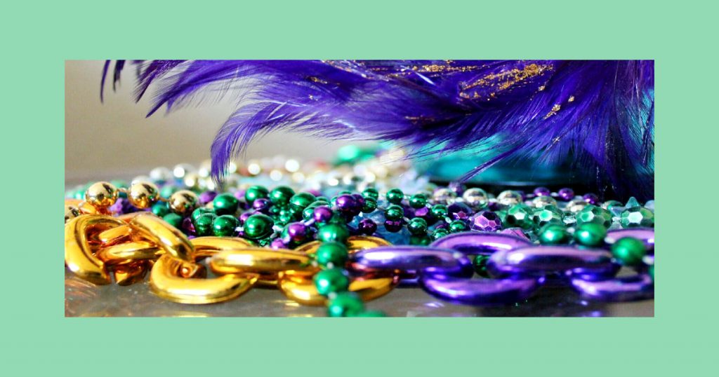 Purple, green, gold, and silver beads and chains with purple feathers in the background