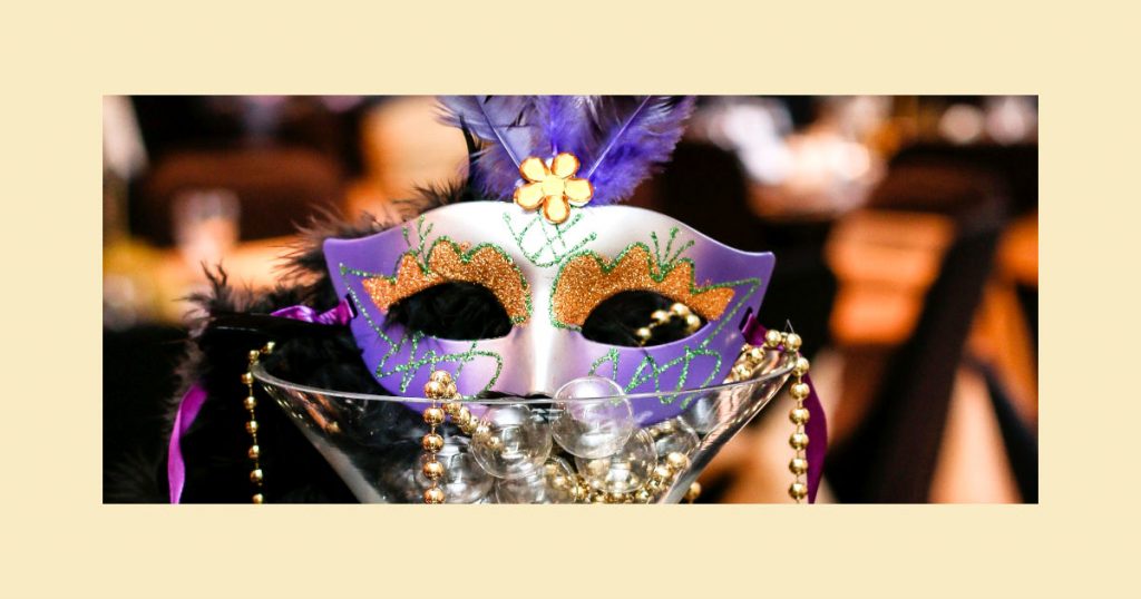 A purple mask with gold decorations in an over-sized martini glass