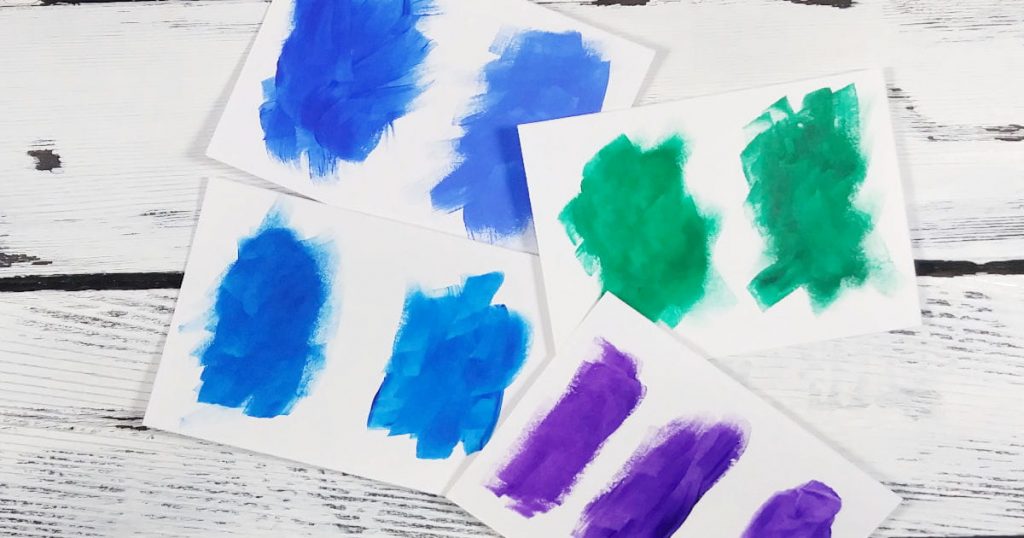 Blue, green, and purple paint swatches on a white wooden background