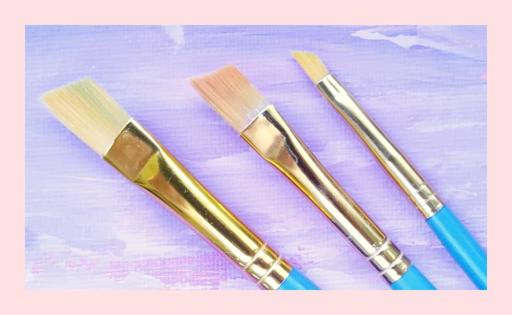 Angled paintbrushes against a purple and pink painted background.