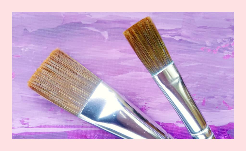 Flat paintbrushes against a purple painted background. Choosing your brushes wisely can really help you save money on painting supplies.