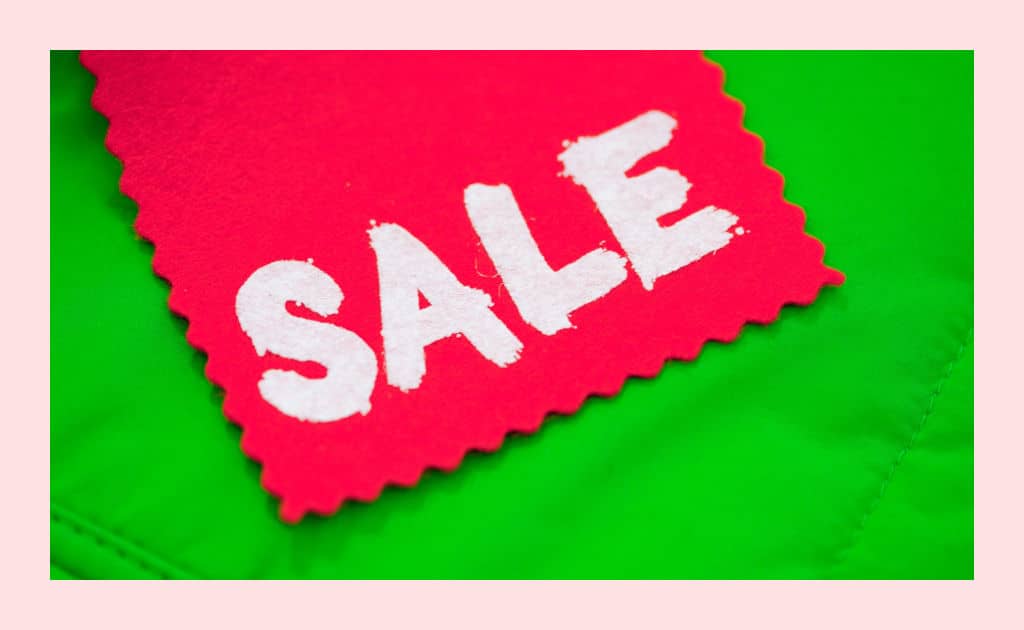A bright pink piece of fabric with the word "SALE" written on it in white paint, laying on a lime green fabric background.