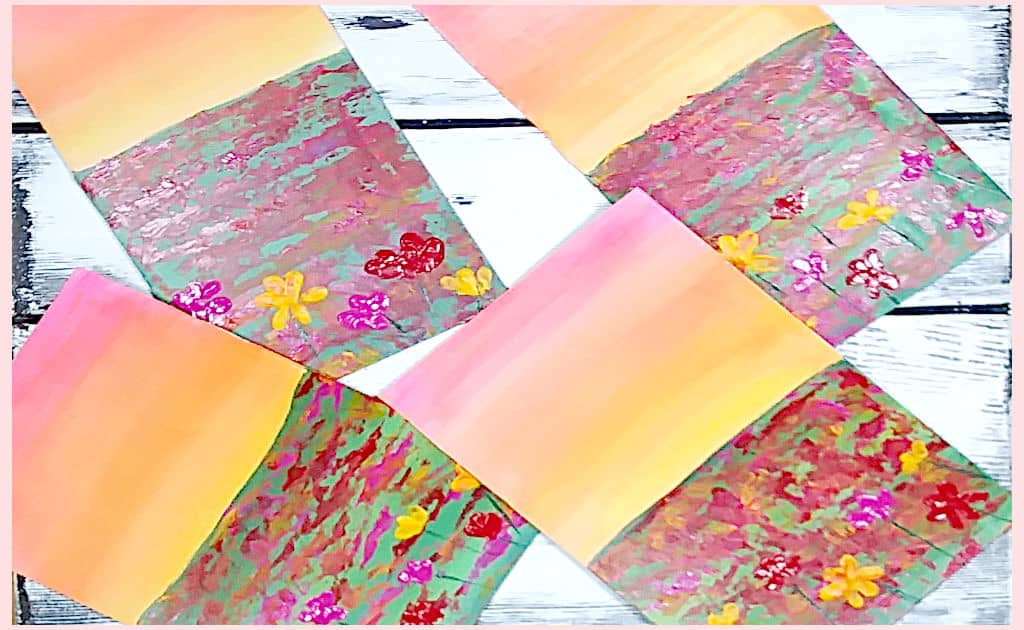 Two pieces of corrugated cardboard, one primed with gesso and one with white paint, with a sunset lit flower field painted on them, and two piece of paperboard, one primed with gesso and one with white paint, with the same painting on both to show the results of the experiment to see what happens when you put acrylic paint on cardboard.