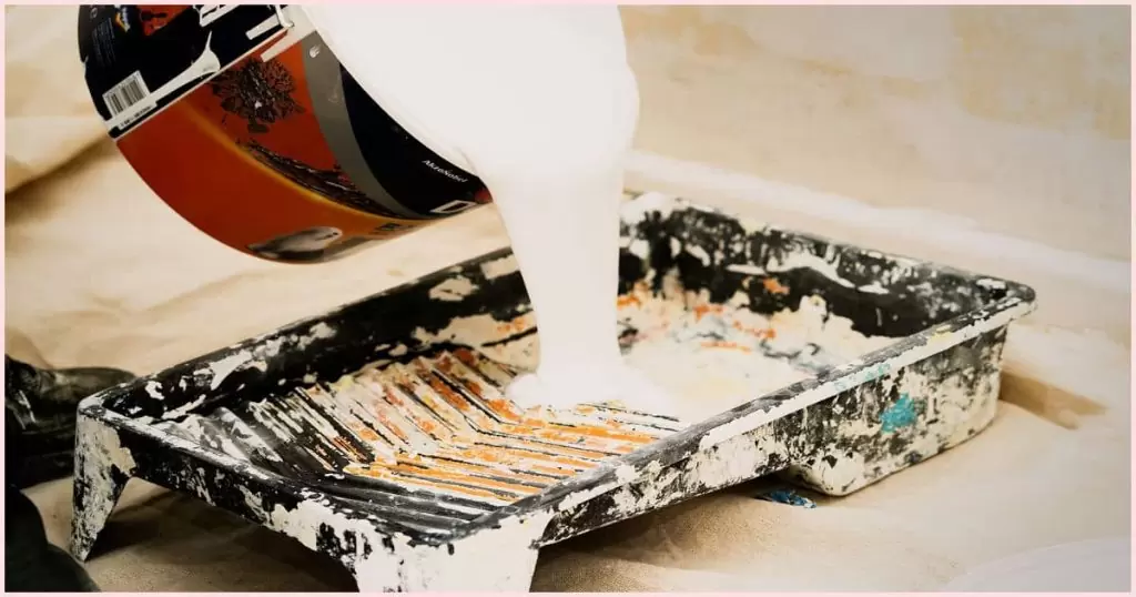 White paint being poured from a can into a roller tray.