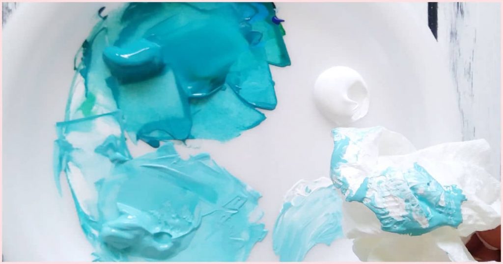 Turquoise paint on a white palette and a piece of paper towel with the same color on it.