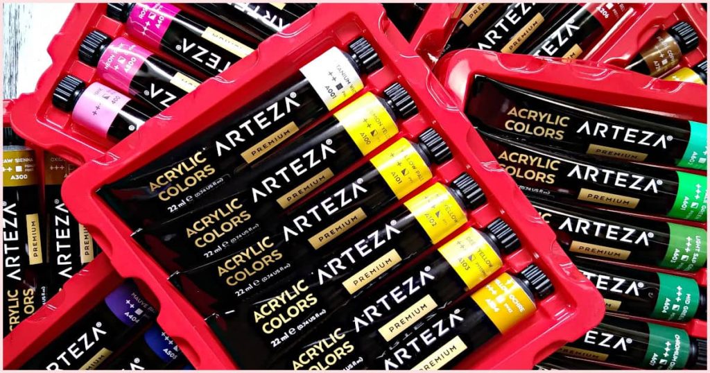 My collection of Arteza Premium acrylic paint. Sixty tubes of different colored paint, in red trays, stacked haphazardly.