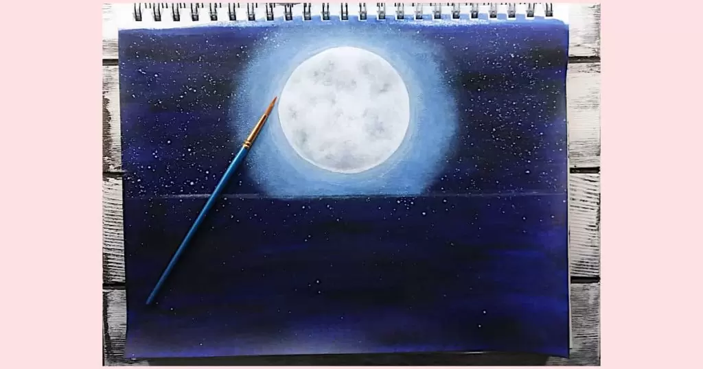 A small detail round brush laying on top of the moon painting tutorial. This brush is used to add the darkest parts of the craters, the pale yellow for the lighter parts of the moon, and the white to pump up the brightness of the moon.