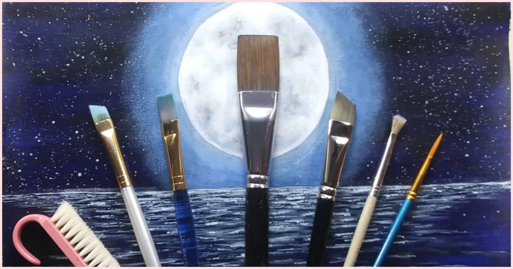 Paintbrushes of different sizes and shapes laying on top of the finished moon painting tutorial.