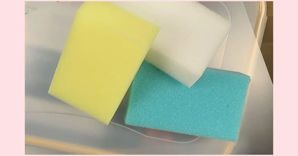 A clear plastic container with white, turquoise, and yellow sponges piled inside