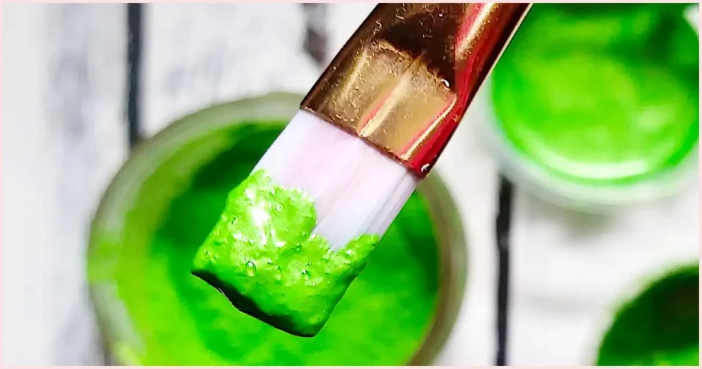 Lime green mica paint on the end of a white bristled acrylic paint brush.