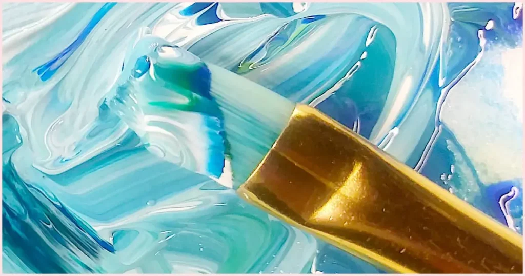 Blue, green, and white paint marbled on a paint brush. Having different sizes of the same shape is part of choosing the right acrylic paint brushes for beginners.