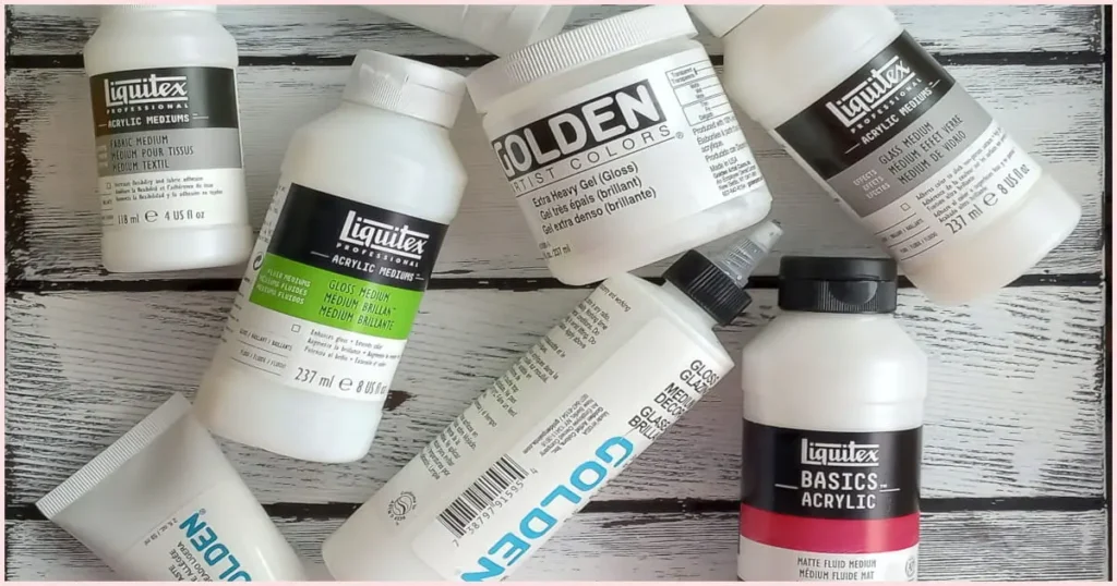An assortment of acrylic mediums laying on a white wooden background.