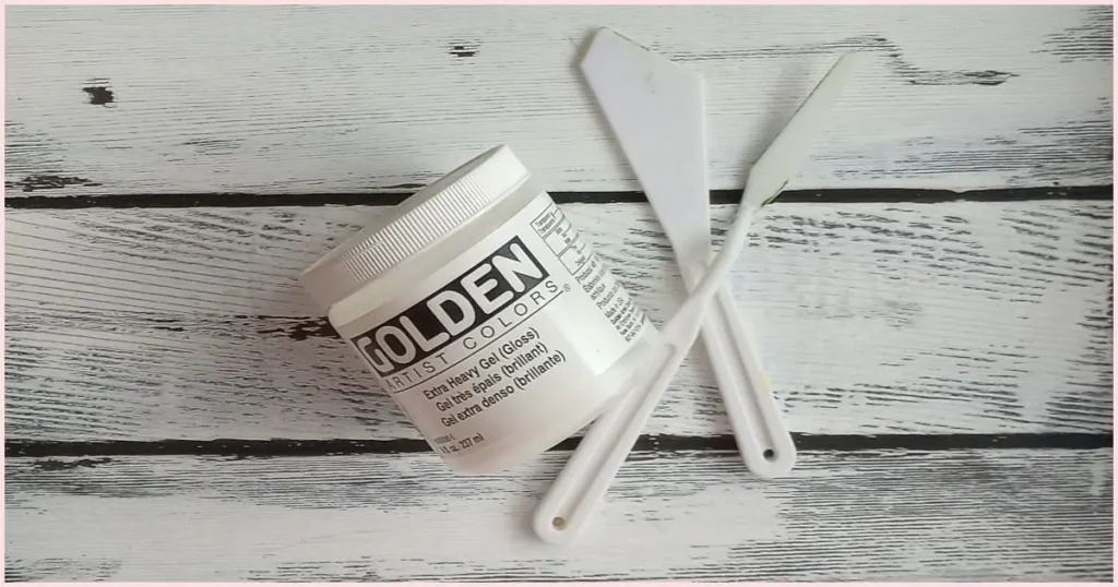 A jar of Extra Heavy Gel acrylic medium and two different shaped white plastic palette knives.