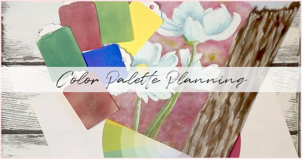 A painting of a distant flower field with a close-up of a weathered fence post with white flowers crowding around the base of it. Scattered next to it are various paint chips to demonstrate how to use a color wheel to plan your color palette.